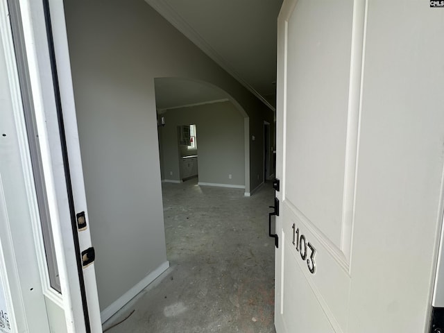 hall with arched walkways, lofted ceiling, concrete floors, baseboards, and ornamental molding