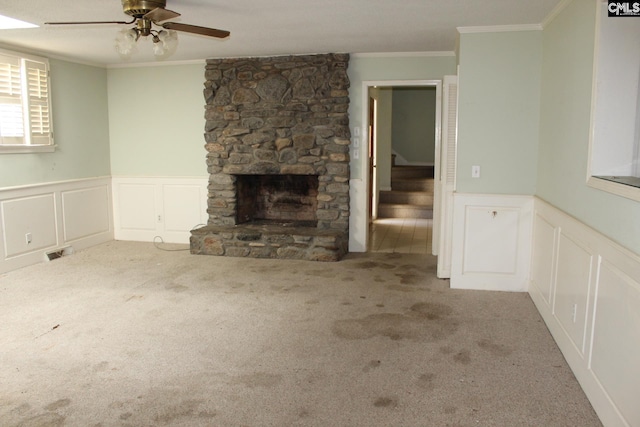 unfurnished living room with ceiling fan, ornamental molding, light colored carpet, and a stone fireplace