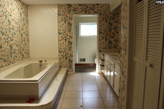 bathroom with toilet, tile patterned flooring, vanity, and tiled bath