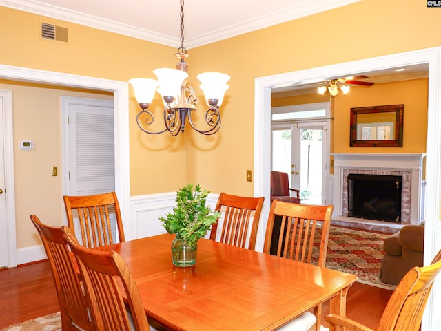 dining space with ceiling fan with notable chandelier, hardwood / wood-style flooring, a fireplace, and crown molding