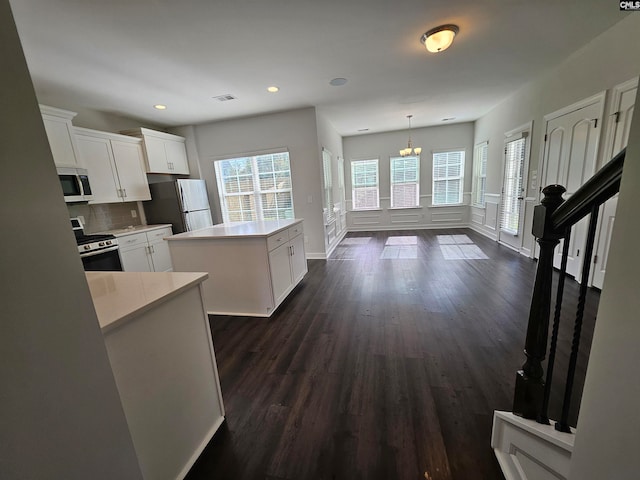 kitchen featuring hanging light fixtures, white cabinets, backsplash, a kitchen island, and appliances with stainless steel finishes