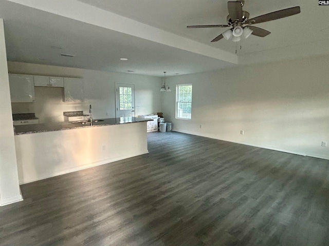 unfurnished living room with ceiling fan with notable chandelier, dark wood-type flooring, and sink