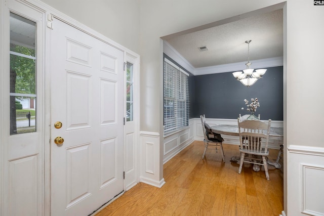 entryway with light hardwood / wood-style floors, ornamental molding, and a chandelier