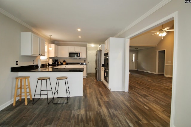kitchen with appliances with stainless steel finishes, a peninsula, ornamental molding, baseboards, and dark wood-style floors