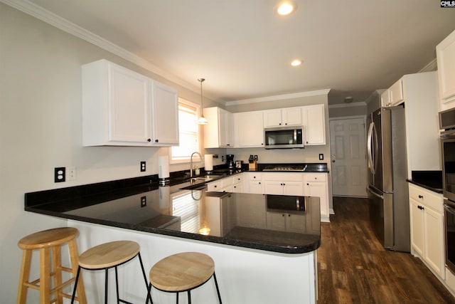 kitchen with appliances with stainless steel finishes, a sink, a peninsula, crown molding, and dark wood-type flooring