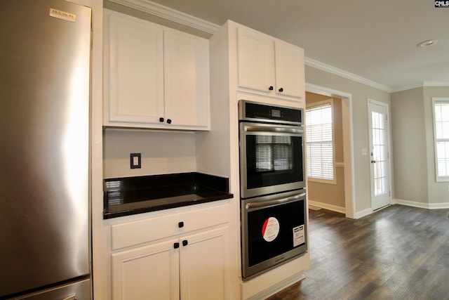 kitchen featuring stainless steel appliances, dark countertops, dark wood finished floors, crown molding, and white cabinetry