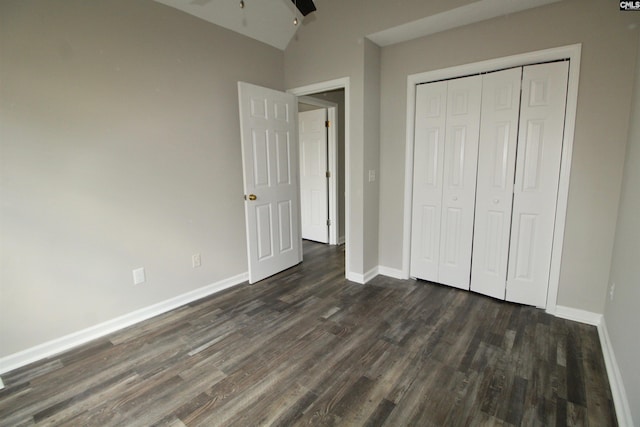unfurnished bedroom with dark wood-style flooring, baseboards, lofted ceiling, and a closet