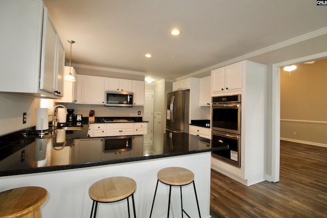 kitchen featuring stainless steel appliances, a sink, ornamental molding, a peninsula, and dark wood-type flooring