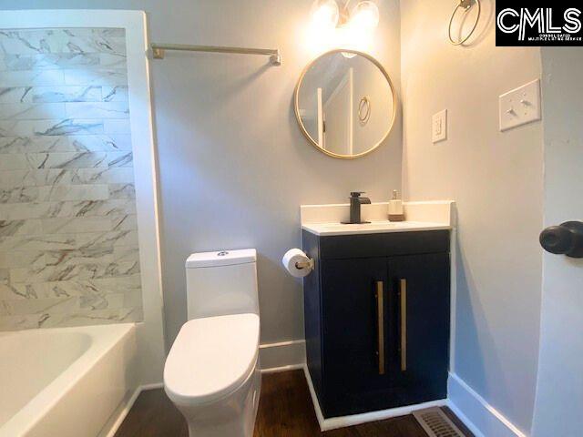 full bathroom with hardwood / wood-style floors, tiled shower / bath combo, vanity, and toilet