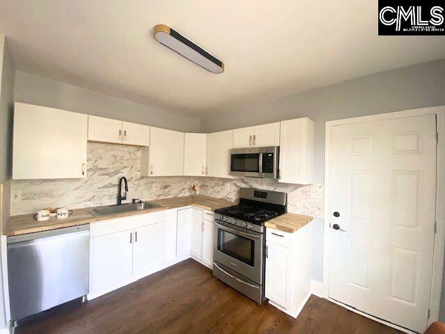 kitchen featuring appliances with stainless steel finishes, white cabinetry, tasteful backsplash, dark hardwood / wood-style flooring, and sink