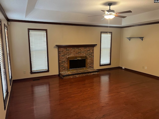 unfurnished living room with a tray ceiling, dark hardwood / wood-style floors, a brick fireplace, ornamental molding, and ceiling fan