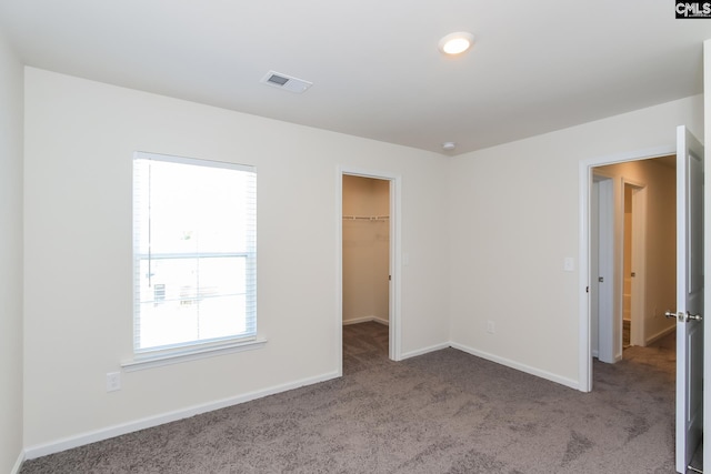 unfurnished bedroom with light colored carpet, a closet, multiple windows, and a walk in closet