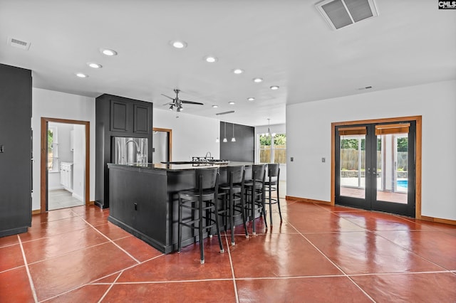 kitchen featuring ceiling fan, french doors, a kitchen island with sink, stainless steel refrigerator, and a kitchen breakfast bar