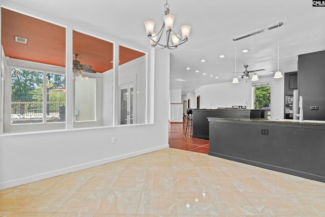 kitchen with ceiling fan with notable chandelier, tile patterned flooring, pendant lighting, and dark stone counters