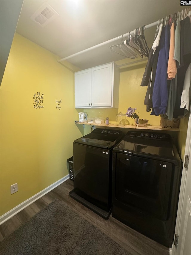 clothes washing area featuring washing machine and dryer, dark wood-type flooring, and cabinets