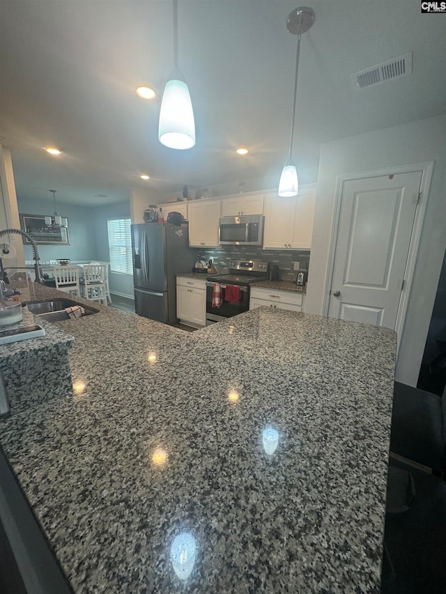 kitchen with hanging light fixtures, appliances with stainless steel finishes, backsplash, and white cabinetry