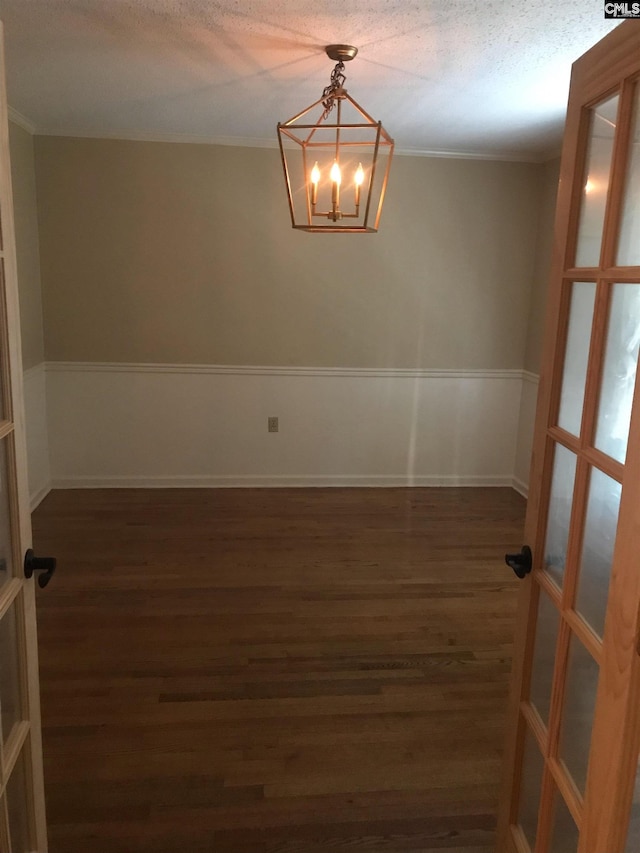 empty room featuring crown molding, dark wood-type flooring, a chandelier, and a textured ceiling