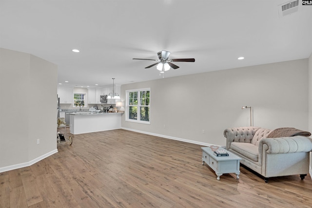 living area with ceiling fan with notable chandelier and light hardwood / wood-style flooring