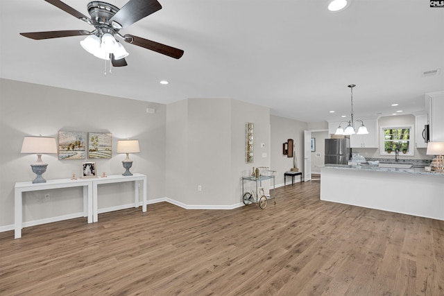 unfurnished living room with ceiling fan with notable chandelier and hardwood / wood-style flooring