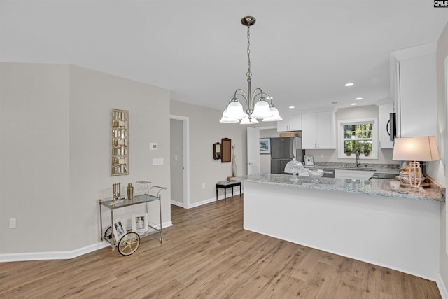 kitchen featuring pendant lighting, light hardwood / wood-style flooring, stainless steel appliances, kitchen peninsula, and white cabinetry