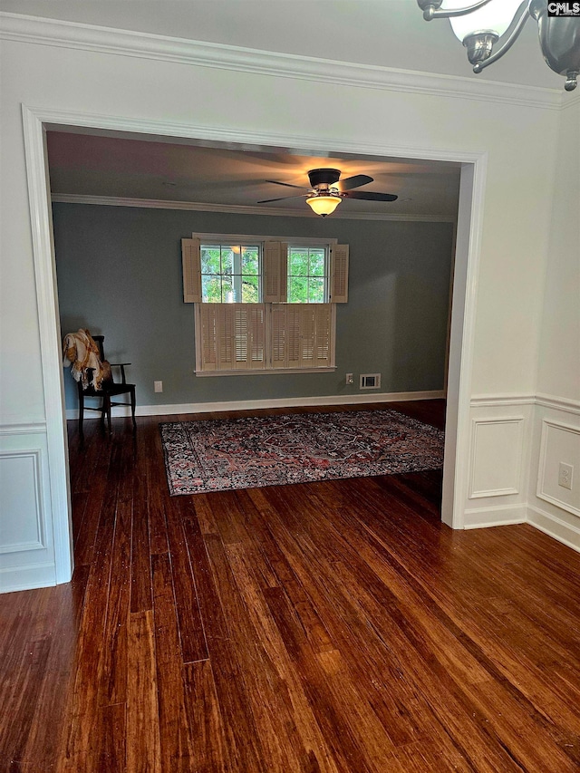 empty room featuring ornamental molding, ceiling fan with notable chandelier, and dark wood-type flooring