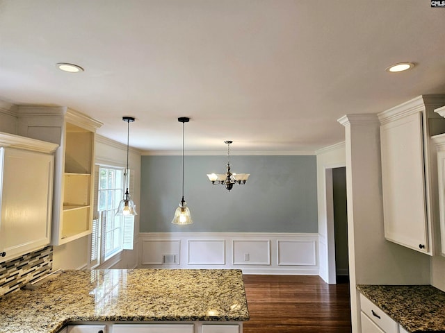 kitchen with dark wood-type flooring, crown molding, decorative light fixtures, and stone countertops