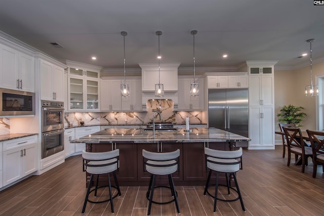 kitchen with an island with sink, hanging light fixtures, stone countertops, appliances with stainless steel finishes, and a kitchen bar