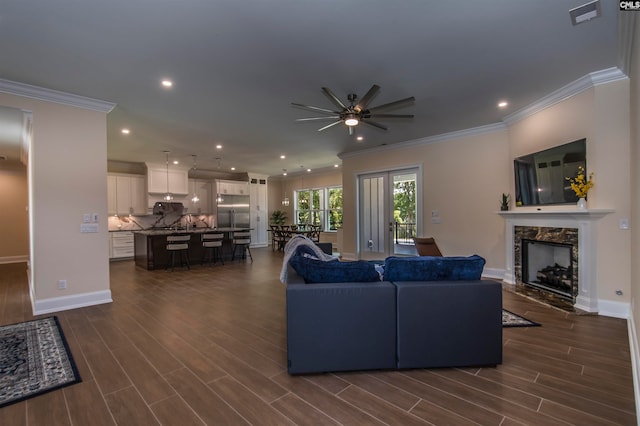 living room with a fireplace, crown molding, dark wood-type flooring, and ceiling fan