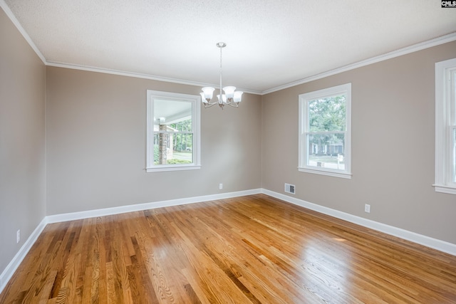 empty room featuring crown molding, a wealth of natural light, an inviting chandelier, and light hardwood / wood-style floors