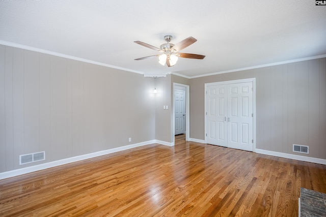 unfurnished bedroom with wood walls, ornamental molding, light hardwood / wood-style flooring, and ceiling fan