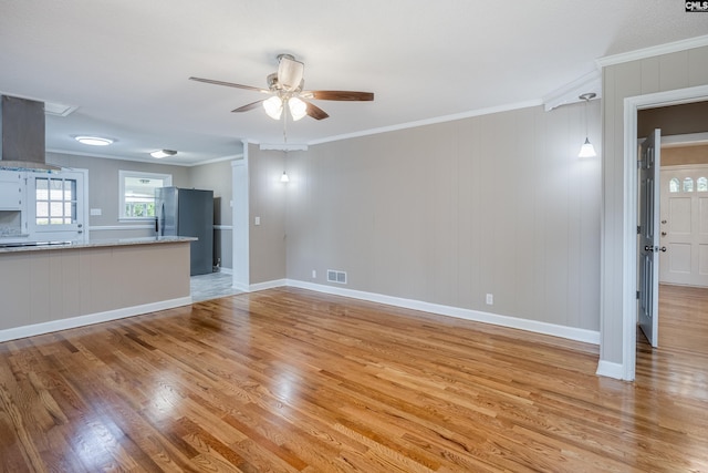 unfurnished living room featuring crown molding, ceiling fan, wood walls, and light hardwood / wood-style flooring