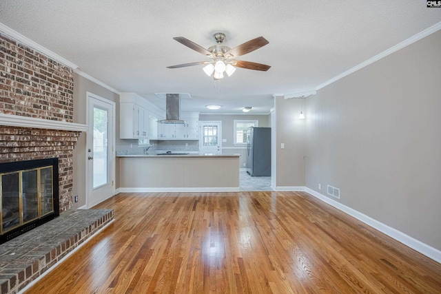 unfurnished living room featuring ornamental molding, a brick fireplace, plenty of natural light, and light hardwood / wood-style floors