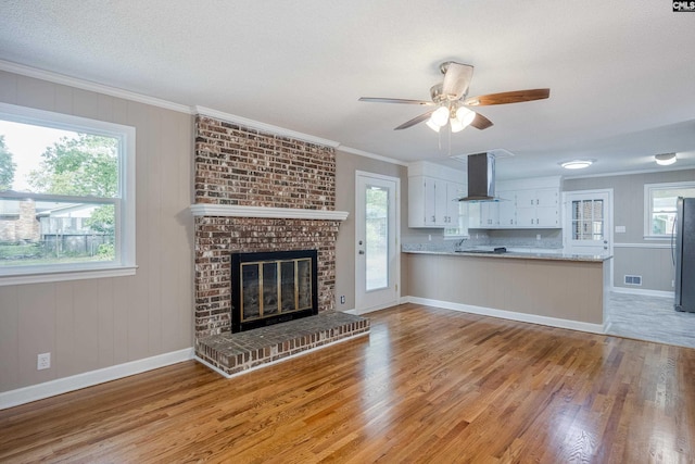 unfurnished living room featuring ceiling fan, ornamental molding, a brick fireplace, wooden walls, and light wood-type flooring