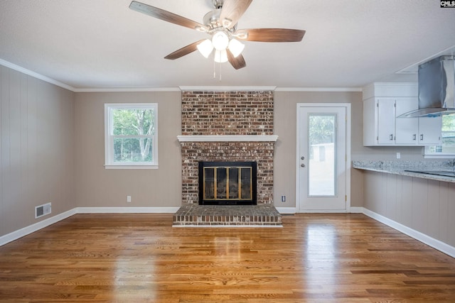 unfurnished living room with ceiling fan, a brick fireplace, wooden walls, hardwood / wood-style flooring, and crown molding