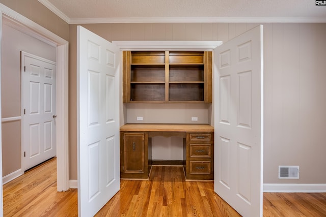 unfurnished office with ornamental molding, built in desk, and light hardwood / wood-style floors