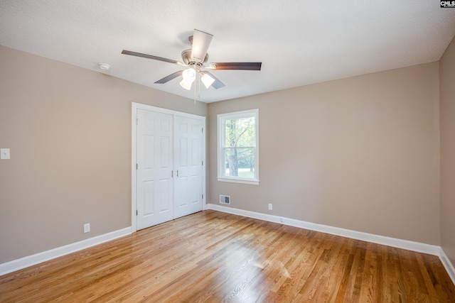 unfurnished bedroom with ceiling fan, a closet, light hardwood / wood-style floors, and a textured ceiling