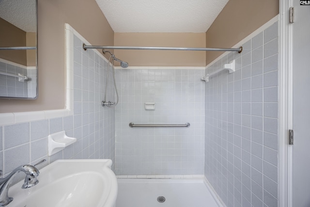 bathroom featuring sink, tile walls, a tile shower, and a textured ceiling