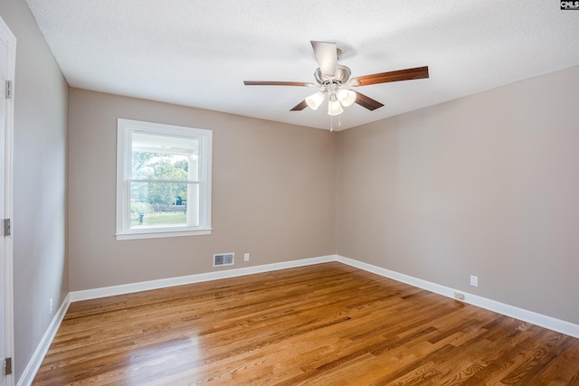 empty room with ceiling fan, light wood-type flooring, and a textured ceiling