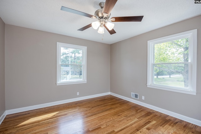 empty room featuring a textured ceiling, light hardwood / wood-style flooring, a wealth of natural light, and ceiling fan