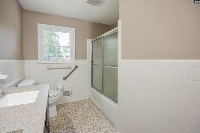 full bathroom featuring vanity, bath / shower combo with glass door, tile walls, tile patterned floors, and toilet