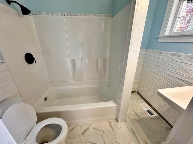 bathroom featuring shower / bathing tub combination, tile walls, and toilet