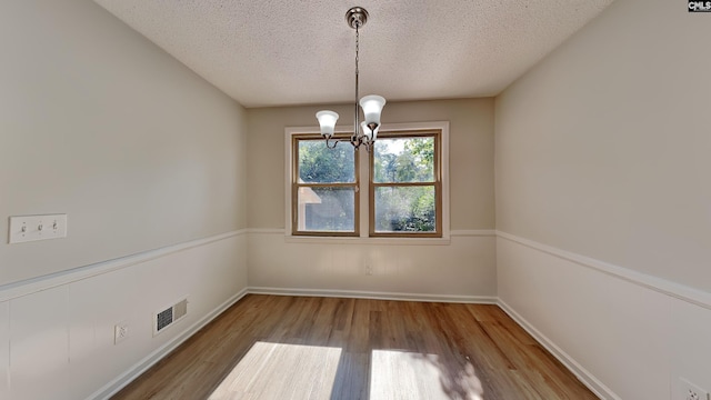 unfurnished room with hardwood / wood-style flooring, a notable chandelier, and a textured ceiling