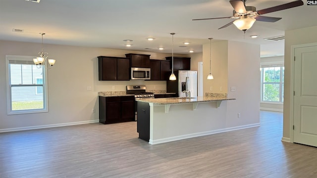 kitchen with a kitchen bar, stainless steel appliances, light wood-type flooring, dark brown cabinets, and light stone countertops