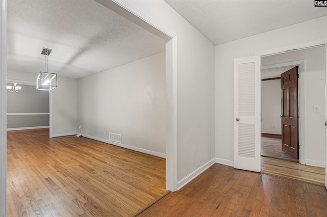 spare room featuring wood-type flooring, a textured ceiling, and a chandelier