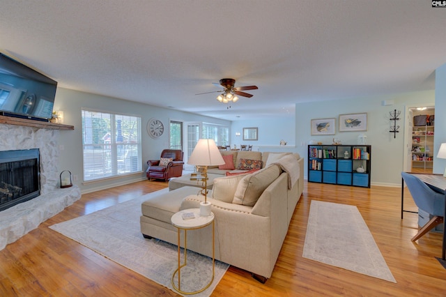 living room featuring a fireplace, light hardwood / wood-style flooring, a textured ceiling, and ceiling fan