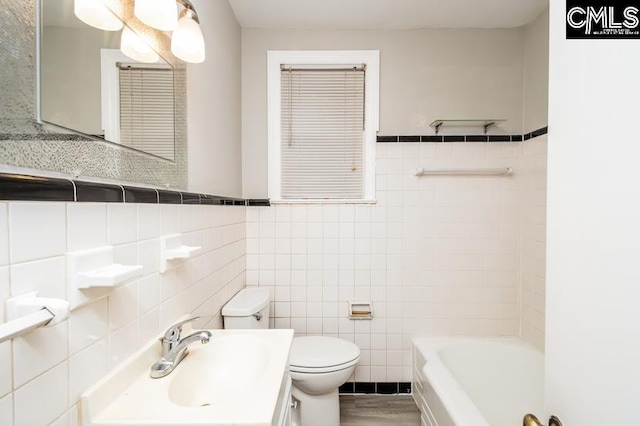 bathroom featuring vanity, tile walls, toilet, and a washtub