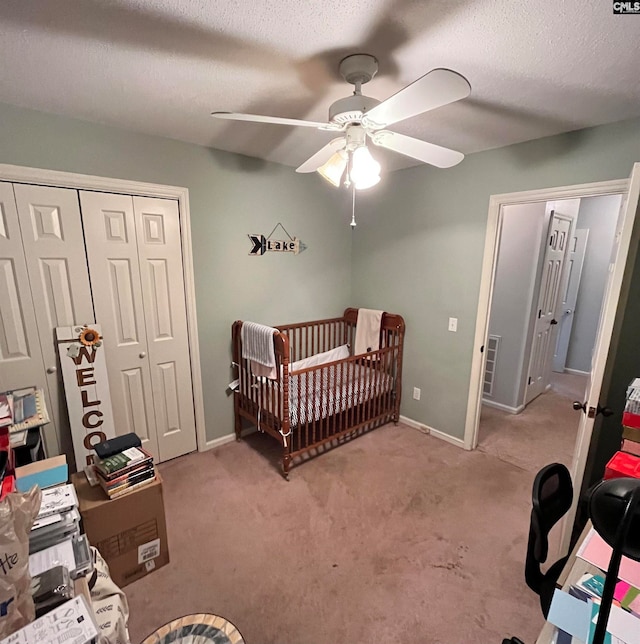 bedroom featuring ceiling fan, a crib, a textured ceiling, a closet, and light colored carpet