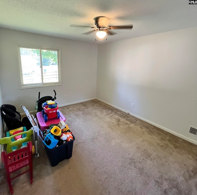 recreation room with carpet flooring, a textured ceiling, and ceiling fan