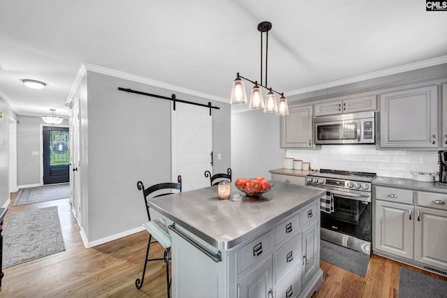 kitchen with a barn door, gray cabinets, light wood-type flooring, stainless steel appliances, and a center island