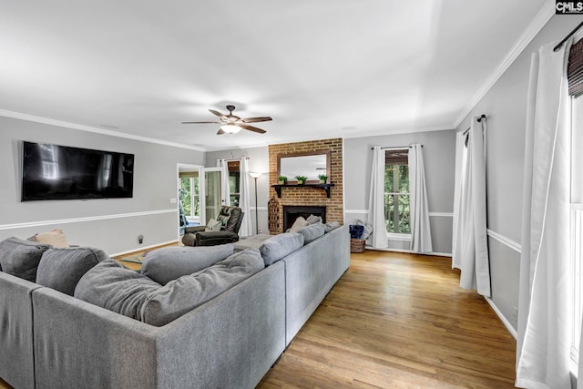 living room with ornamental molding, a brick fireplace, ceiling fan, and light hardwood / wood-style flooring